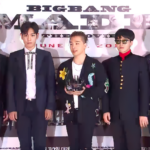 Big Bang members standing behind a table with microphones at a press conference backdrop