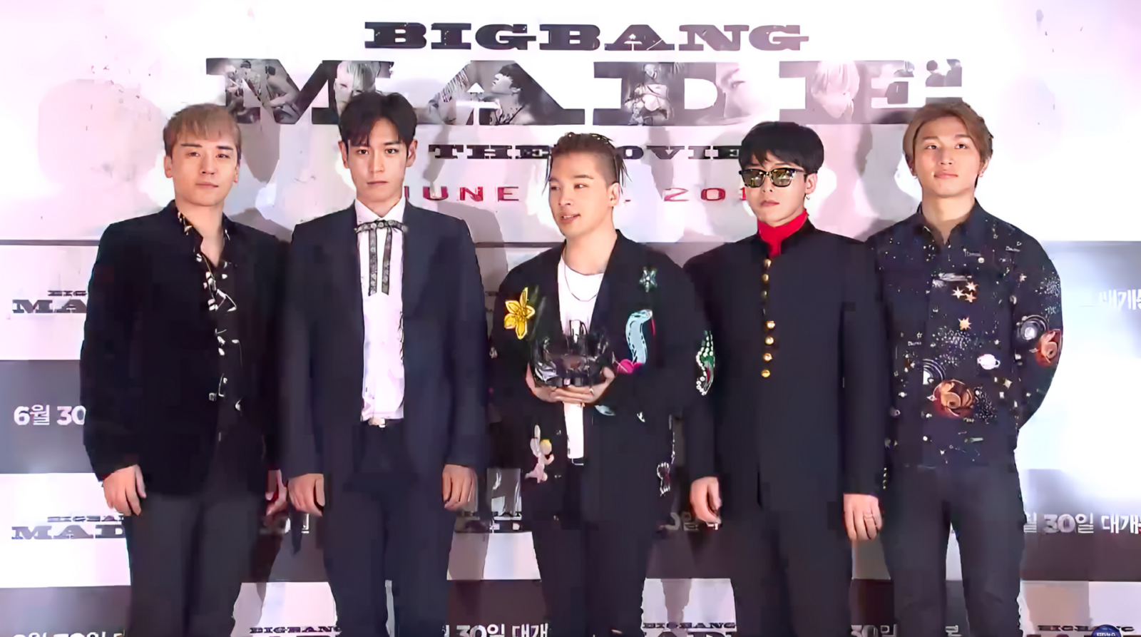 Big Bang members standing behind a table with microphones at a press conference backdrop