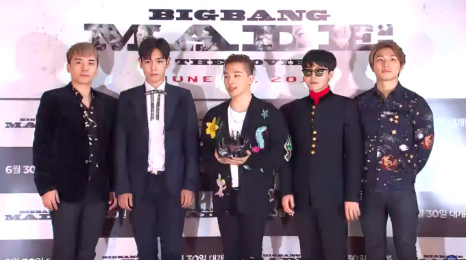 Big Bang members standing behind a table with microphones at a press conference backdrop