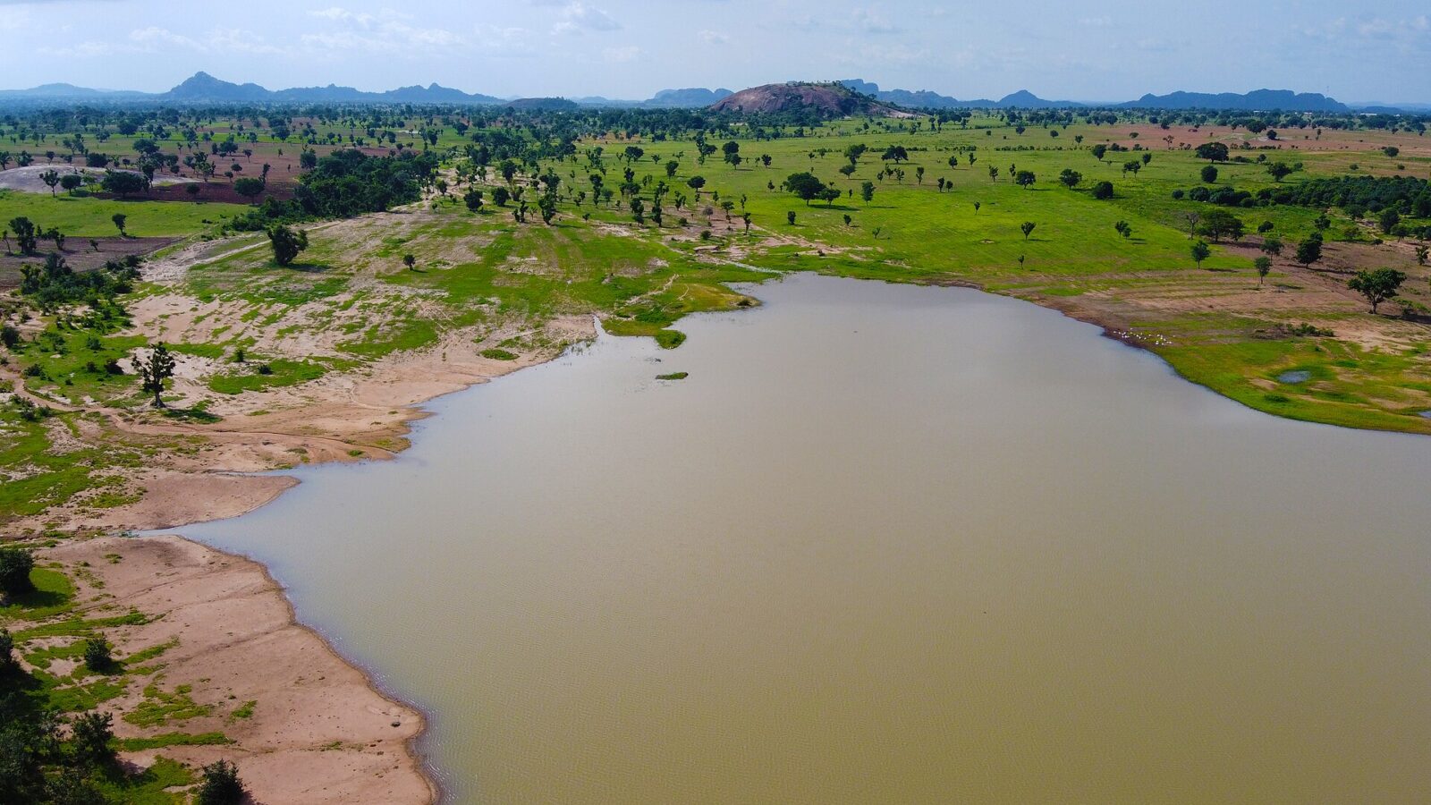 A lake on a farm in Bauchi State, Nigeria with trees and grassy shoreline