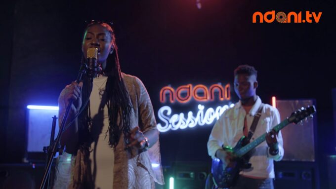 Tems singing into a microphone on stage during a live session